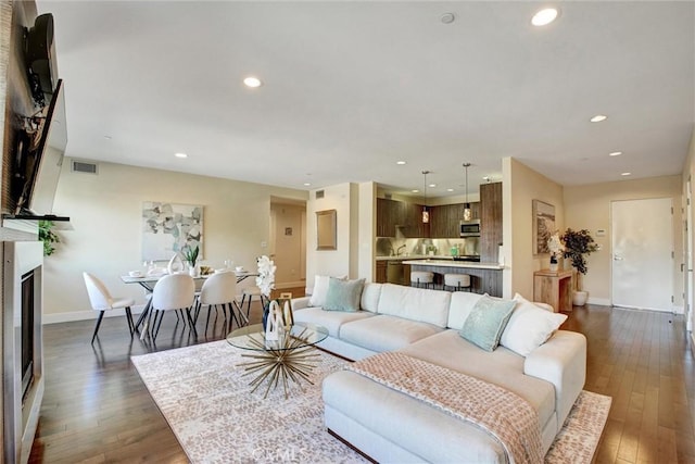 living room with a glass covered fireplace, visible vents, dark wood finished floors, and recessed lighting