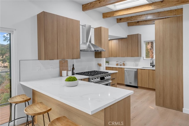 kitchen featuring stainless steel appliances, wall chimney exhaust hood, a skylight, and a kitchen bar