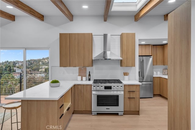 kitchen featuring appliances with stainless steel finishes, light hardwood / wood-style flooring, kitchen peninsula, and wall chimney exhaust hood