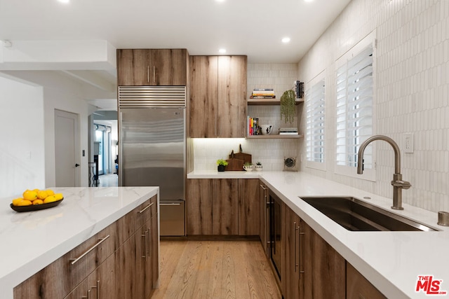 kitchen with stainless steel built in refrigerator, sink, decorative backsplash, and light hardwood / wood-style flooring