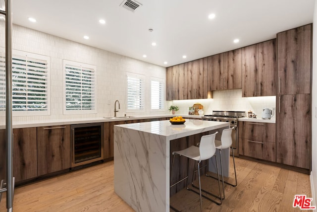 kitchen featuring sink, light hardwood / wood-style flooring, a kitchen island, beverage cooler, and high end stove