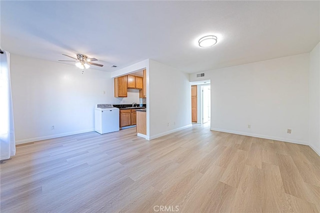 unfurnished living room featuring sink, washer / clothes dryer, ceiling fan, and light hardwood / wood-style flooring