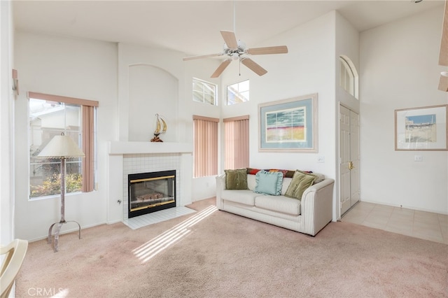 carpeted living room with ceiling fan, a towering ceiling, and a tile fireplace