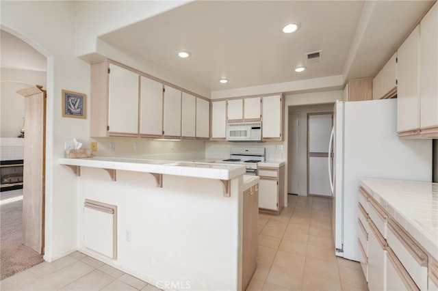 kitchen featuring white appliances, tile counters, a kitchen breakfast bar, and kitchen peninsula