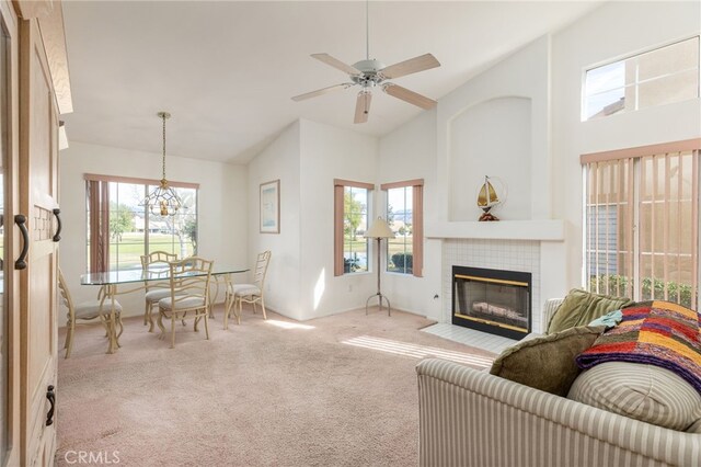 carpeted living room with a tile fireplace, a healthy amount of sunlight, ceiling fan with notable chandelier, and high vaulted ceiling