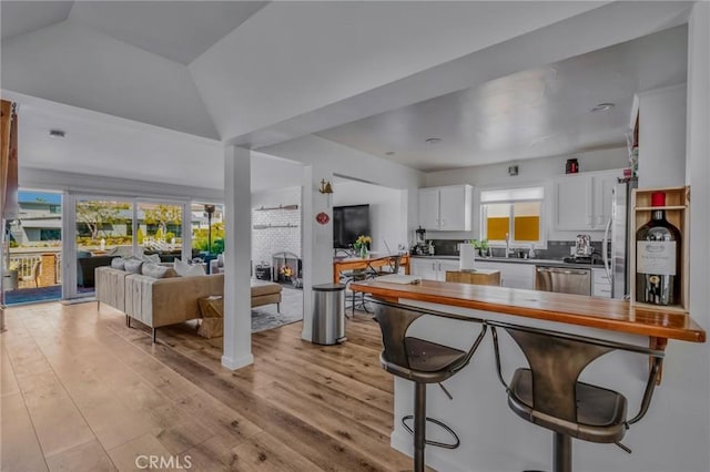 kitchen with vaulted ceiling, decorative backsplash, white cabinetry, a fireplace, and appliances with stainless steel finishes