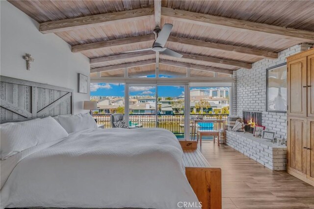 bedroom featuring multiple windows, a fireplace, lofted ceiling with beams, and light hardwood / wood-style floors