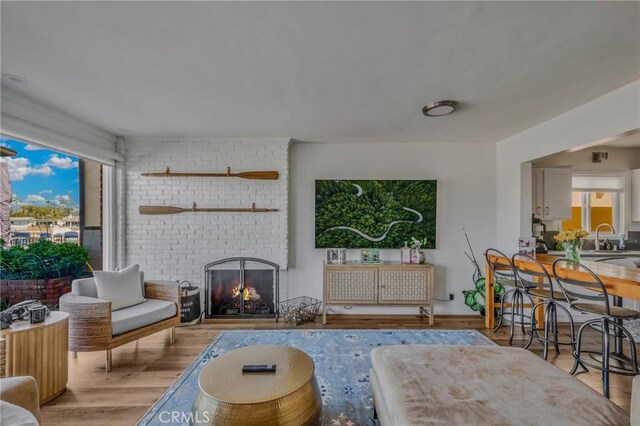 living room with a brick fireplace, light hardwood / wood-style flooring, and sink