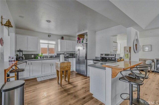 kitchen featuring sink, white cabinets, a kitchen breakfast bar, kitchen peninsula, and appliances with stainless steel finishes