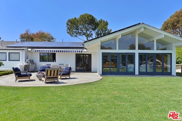 rear view of house featuring solar panels, a patio area, a yard, and an outdoor living space