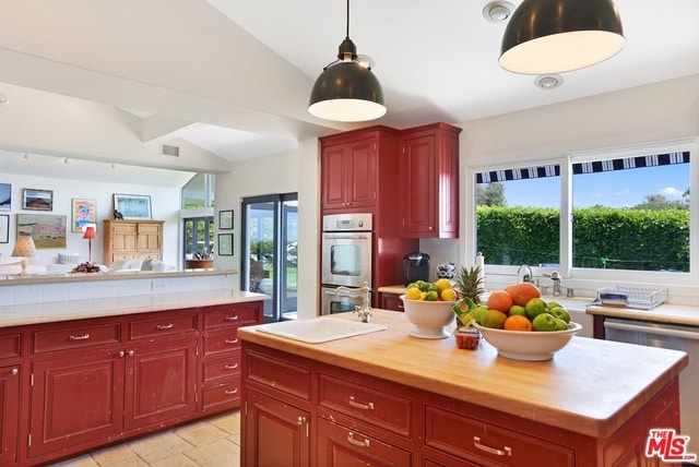 kitchen with stainless steel appliances, sink, lofted ceiling, an island with sink, and hanging light fixtures