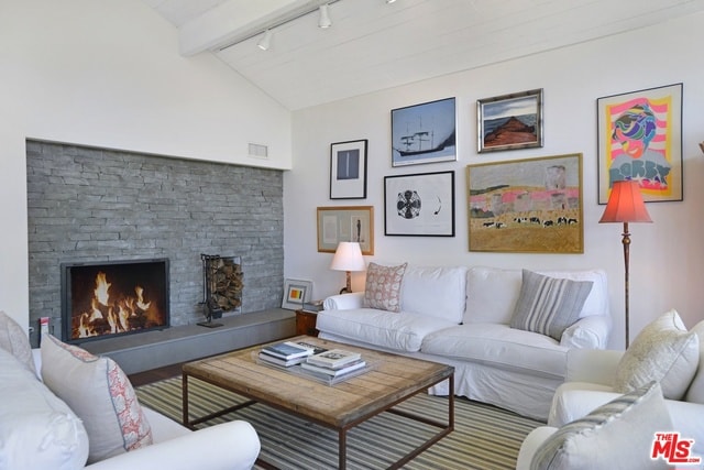 living room with rail lighting, lofted ceiling with beams, and a stone fireplace