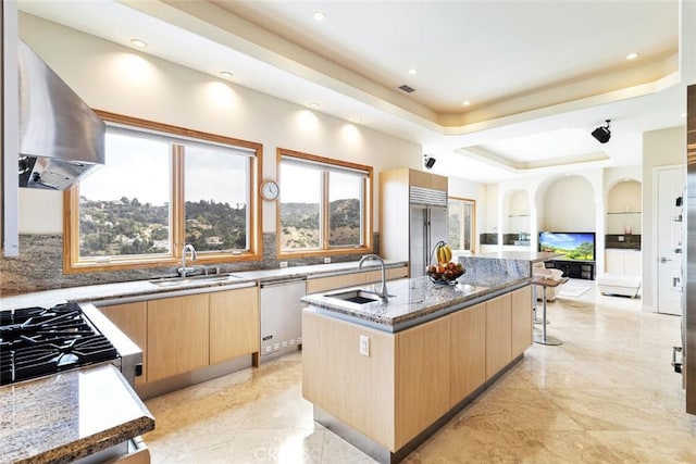 kitchen with sink, an island with sink, stone countertops, extractor fan, and appliances with stainless steel finishes