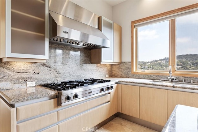 kitchen featuring sink, stainless steel gas stovetop, light brown cabinetry, light stone countertops, and wall chimney range hood