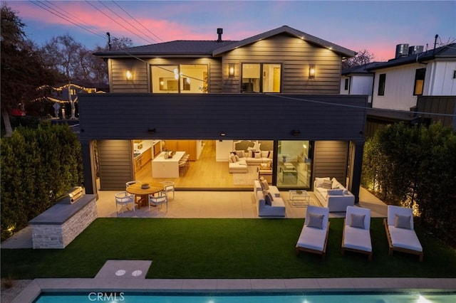 back of property at dusk featuring an outdoor living space, a patio, and a lawn