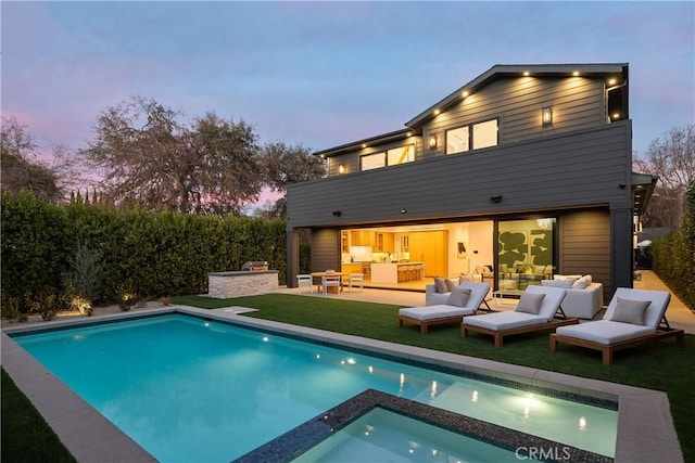 back of property at dusk with a patio, a pool with connected hot tub, outdoor lounge area, and area for grilling