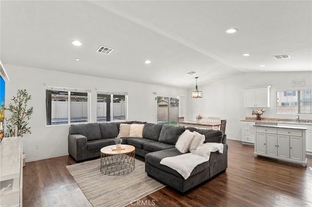 living room featuring lofted ceiling, dark hardwood / wood-style flooring, a chandelier, and sink