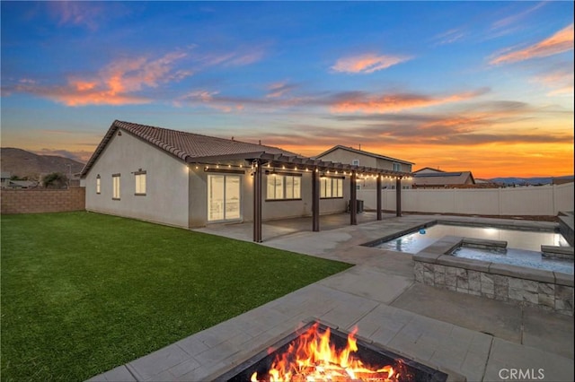 pool at dusk with a yard, a fire pit, a patio, and an in ground hot tub