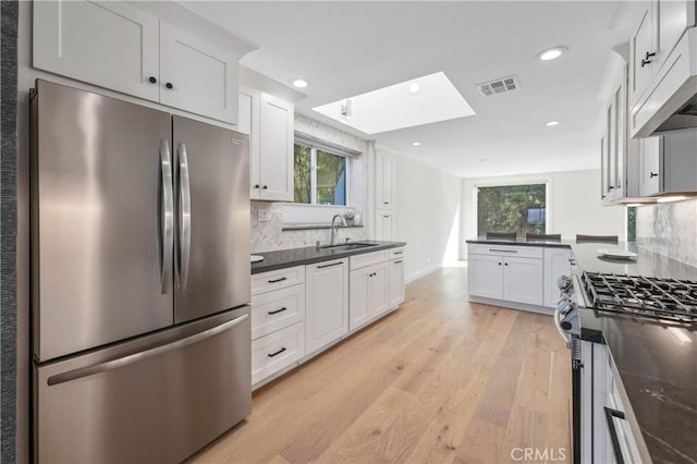 kitchen featuring appliances with stainless steel finishes, a skylight, white cabinets, light hardwood / wood-style flooring, and sink