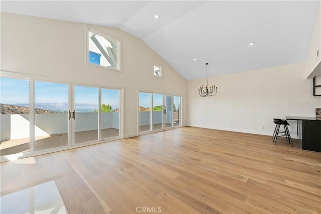 unfurnished living room with high vaulted ceiling, an inviting chandelier, a wealth of natural light, and light hardwood / wood-style flooring