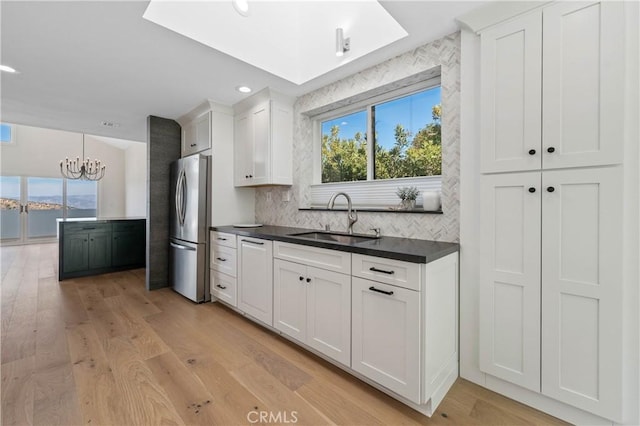 kitchen with a chandelier, stainless steel fridge, tasteful backsplash, white cabinetry, and sink