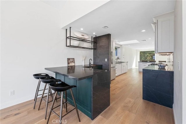 kitchen featuring sink, white cabinetry, light hardwood / wood-style floors, kitchen peninsula, and a breakfast bar