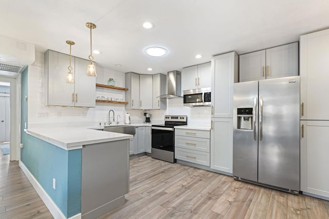 kitchen with stainless steel appliances, hanging light fixtures, sink, wall chimney range hood, and tasteful backsplash