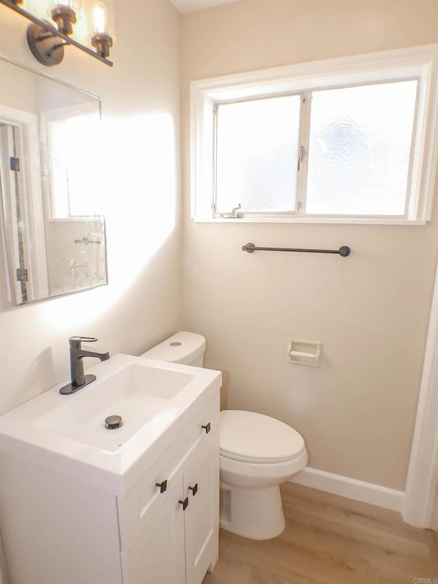 bathroom with toilet, wood-type flooring, vanity, and a wealth of natural light