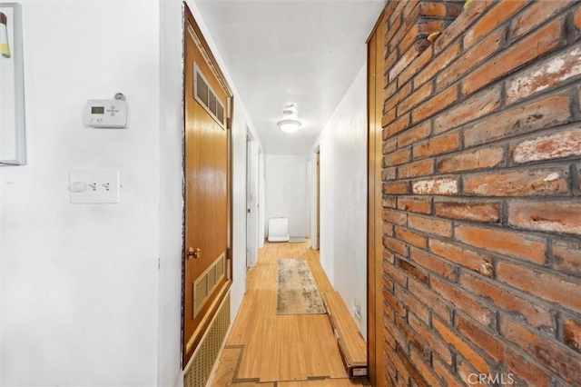 corridor featuring brick wall and light wood-type flooring