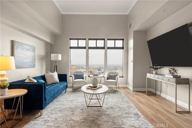 living area featuring visible vents, ornamental molding, wood finished floors, a high ceiling, and baseboards