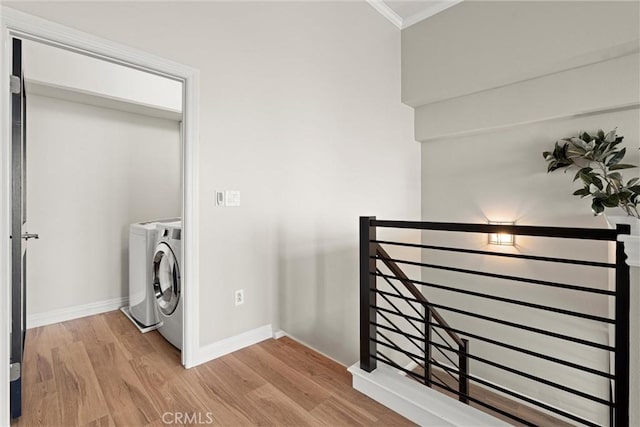 laundry area featuring baseboards, light wood finished floors, washing machine and clothes dryer, laundry area, and crown molding