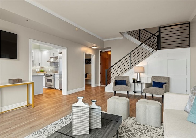 living room featuring crown molding, light wood-type flooring, stairs, and baseboards