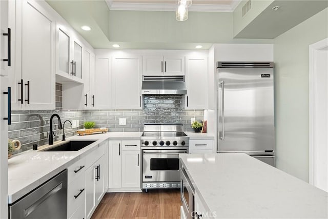 kitchen featuring visible vents, ornamental molding, under cabinet range hood, a sink, and built in appliances