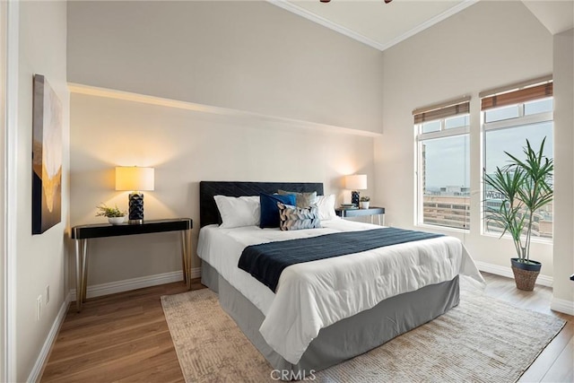 bedroom featuring wood finished floors, baseboards, a towering ceiling, and ornamental molding