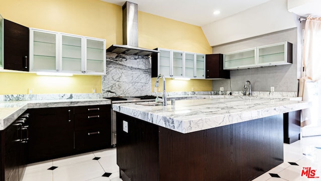 kitchen featuring sink, light tile patterned floors, a breakfast bar area, an island with sink, and wall chimney exhaust hood