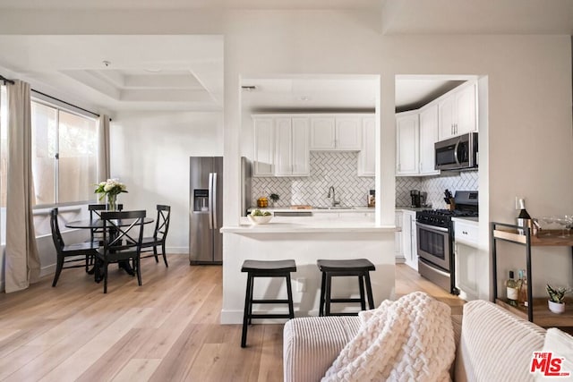 kitchen with appliances with stainless steel finishes, light hardwood / wood-style floors, a breakfast bar, white cabinets, and sink