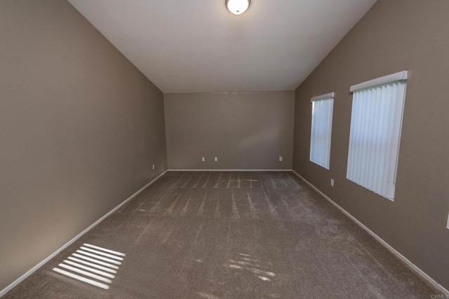 unfurnished room with lofted ceiling and dark colored carpet