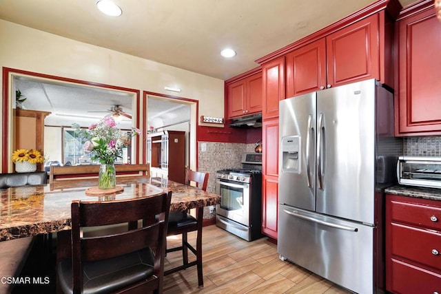 kitchen with dark stone countertops, light wood-type flooring, backsplash, appliances with stainless steel finishes, and ceiling fan