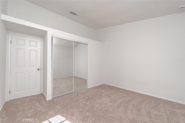 unfurnished bedroom with light colored carpet and a closet