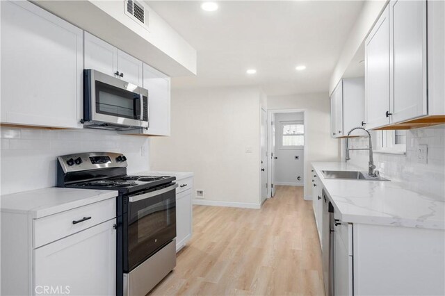 kitchen with appliances with stainless steel finishes, light hardwood / wood-style floors, light stone countertops, white cabinets, and sink