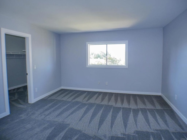 unfurnished bedroom featuring a spacious closet, a closet, and dark colored carpet