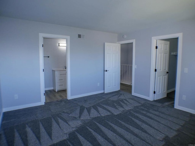 unfurnished bedroom featuring dark colored carpet, a closet, connected bathroom, and a spacious closet