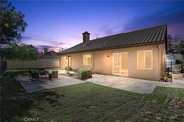 back house at dusk with a patio and a lawn