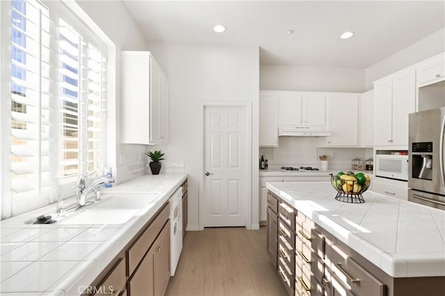 kitchen featuring sink, white cabinetry, tile countertops, white appliances, and light hardwood / wood-style flooring