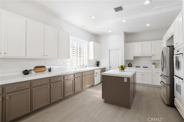 kitchen featuring white appliances, a center island, decorative backsplash, light wood-type flooring, and white cabinets