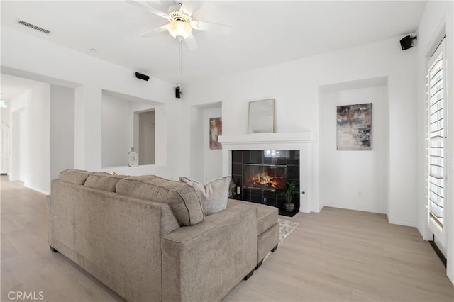 living room with a fireplace, ceiling fan, a wealth of natural light, and light hardwood / wood-style flooring