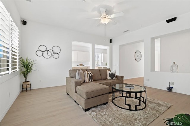 living room featuring light wood-type flooring, ceiling fan, and a healthy amount of sunlight