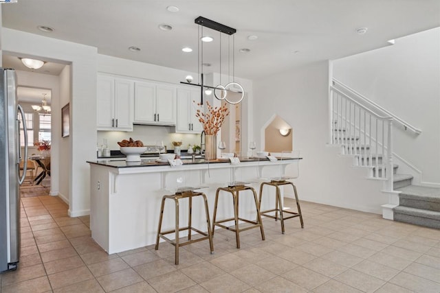 kitchen featuring hanging light fixtures, light tile patterned floors, a breakfast bar, stainless steel refrigerator, and white cabinets