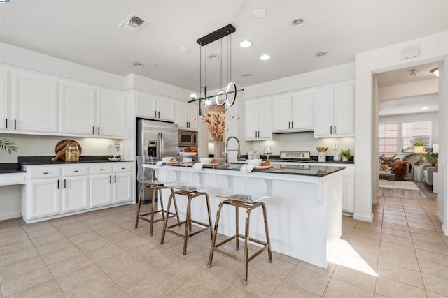 kitchen featuring pendant lighting, stainless steel appliances, light tile patterned floors, a kitchen island with sink, and white cabinets