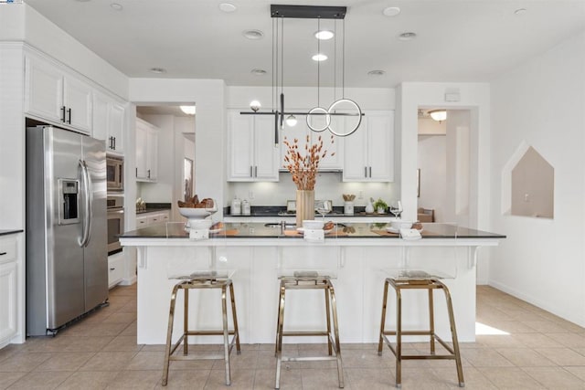 kitchen featuring stainless steel appliances, an island with sink, white cabinetry, and hanging light fixtures